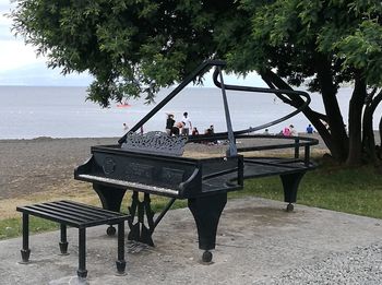 People sitting on bench at beach against sky