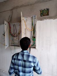 Rear view of man examining electric cables