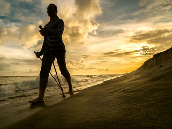 Low angle view of woman walking on shore at beach during sunset