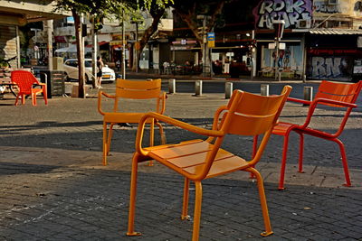 Empty chairs and tables at sidewalk cafe in city