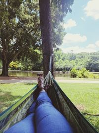 Low section of person on tree trunk against sky