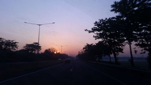 Road by silhouette trees against sky during sunset