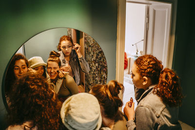 Happy female friends applying make-up in front of mirror at home