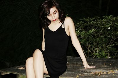 Beautiful young woman sitting on table at night