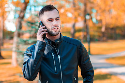 Young man using mobile phone while standing outdoors during autumn