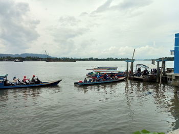 People on boats in river against sky