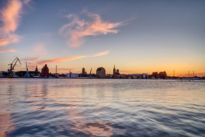 Scenic view of river by buildings against sky during sunset