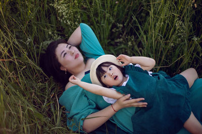 Koreans family mother and daughter in green dresses lie in the long grass on the field at sunset