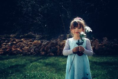 Portrait of girl holding flower while standing in lawn