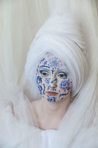 Woman with painted face looking away against curtain at home