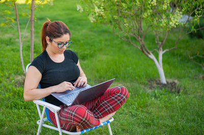 Young woman using phone while sitting on grass