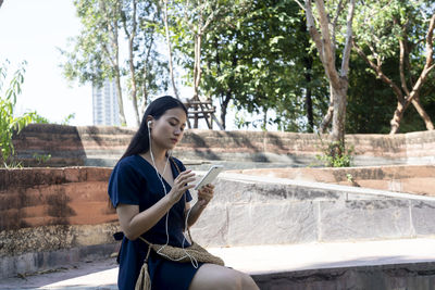 Young woman looking at camera while sitting on retaining wall