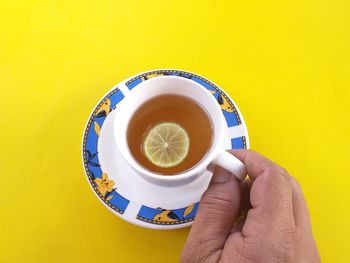 Directly above shot of person holding tea cup against yellow background