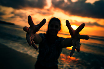 Woman gesturing at beach during sunset