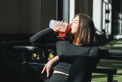 Portrait of resting young brunette woman in sport active wear drinking water in the fitness club