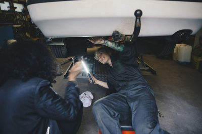 Happy female mechanic looking at customer while examining car at auto repair shop