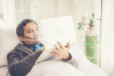 Businessman using laptop while wearing oxygen mask in hospital