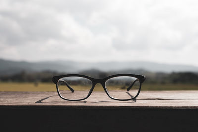 Close-up of eyeglasses on wooden table against sky