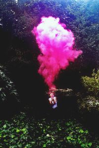 Woman holding pink distress flare in forest