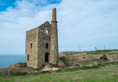 Old building on field by sea against sky