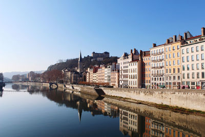 Buildings by river against sky in city