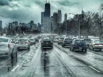 Vehicles on road in city against storm clouds