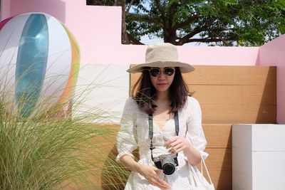 Portrait of young woman wearing hat holding camera