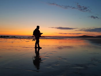 Silhouette man standing on beach against sky during sunset