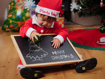 Cute girl holding merry christmas text on blackboard at home