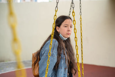 Portrait of girl with face protective mask sitting on a swing