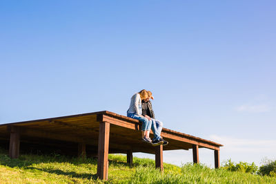 Woman sitting on field against clear blue sky