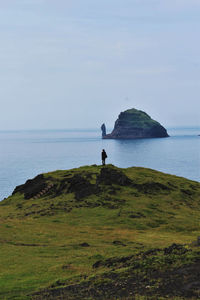 Woman standing on cliff by sea against sky