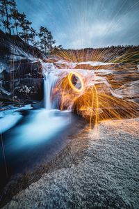 Light trails by waterfall against sky