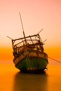 Ferris wheel in sea against orange sky