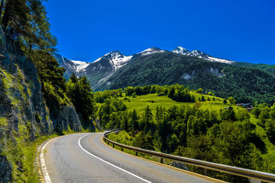 Road leading towards mountains against blue sky