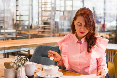 Attractive young businesswoman has a breakfast in a cafe with cup of coffee and sweet porridge.