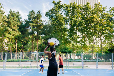 Back view of multiethnic male players with yellow ball while playing basketball on street in sunny day