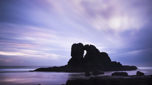 Rock formation on beach against sky during sunset