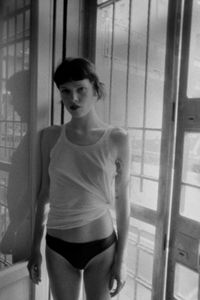 Portrait of young woman standing against window at home