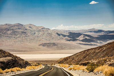 Country road by mountains against sky