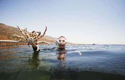 Side view of woman with arms outstretched in sea against clear sky