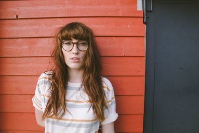 Portrait of young woman wearing eyeglasses standing against brick wall