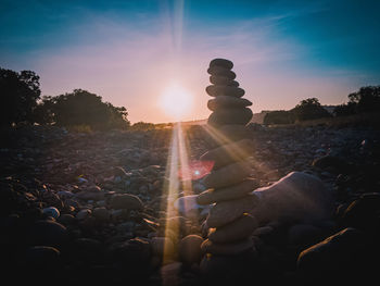 People on rocks at beach against sky during sunset