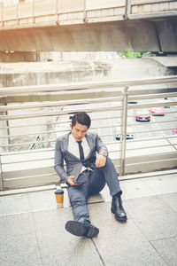 High angle view of businessman using phone while sitting on elevated walkway in city 