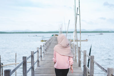 Rear view of woman standing on pier over sea against sky