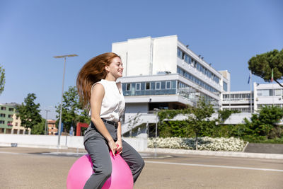 Smiling female freelancer enjoying on bouncy ball on road during sunny day