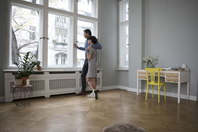 Couple looking together through window at home