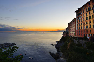 Scenic view of sea by buildings against sky during sunset