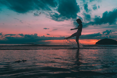 Silhouette young woman splashing water in sea against sky during sunset