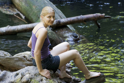 Portrait of smiling young woman sitting on rock at lakeshore